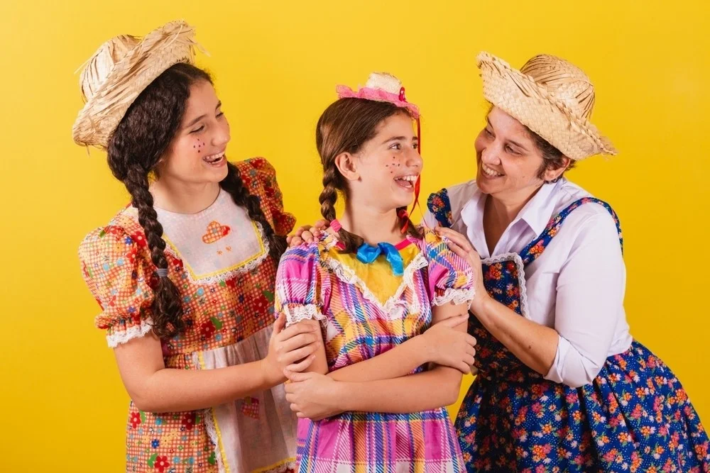 Mulher e duas meninas vestidas com roupas típicas da Festa de São João no Brasil.